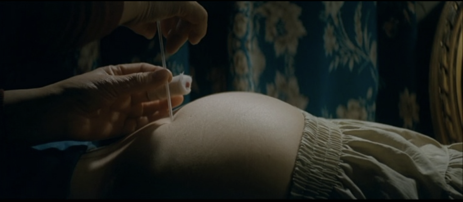 A glass slide pressed to a prosthetic belly in candlelight